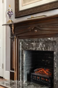 Dark marble fireplace with hand-crafted wooden mantle and electric fire lit