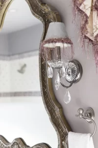 Closeup of antique sconce next to unique mirror in lavender bathroom