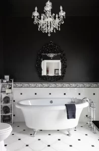 Gorgeous porcelain tub, polished chrome plumbing, and antique chandelier in black and white tile bathroom