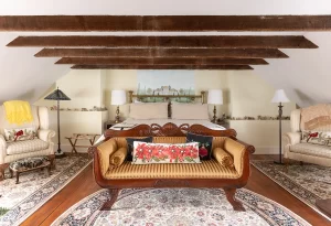 The Frejus bedroom with exposed beam rafters, country estate mural on wall, and seating areas