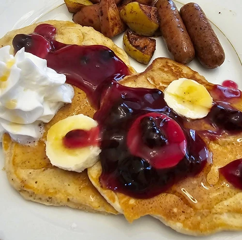 Breakfast of pancakes, fruit, compote, fried potatoes, and sausage at The Richard Johnston Inn