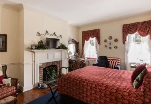 The Virginian patriotic red, white, and blue bedroom with two windows, decorative fireplace, and comfortable seating area